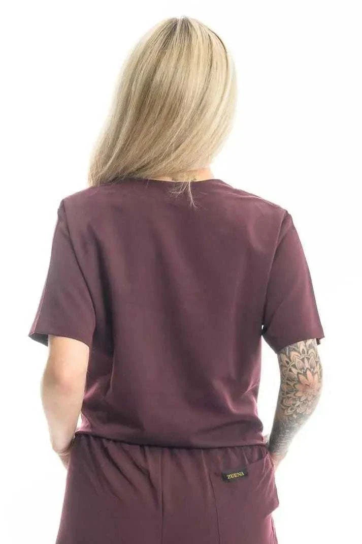 Back view of Zuena Burgundy Bloom short sleeve scrub top with curved neck and side vents worn by person with tattooed arm