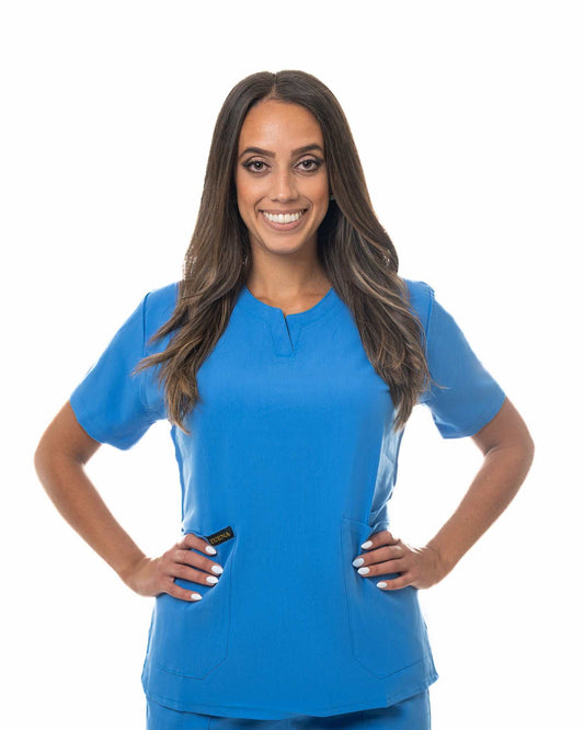 Woman wearing blue Skyward Bound Scrub Top with short sleeves and three pockets, smiling